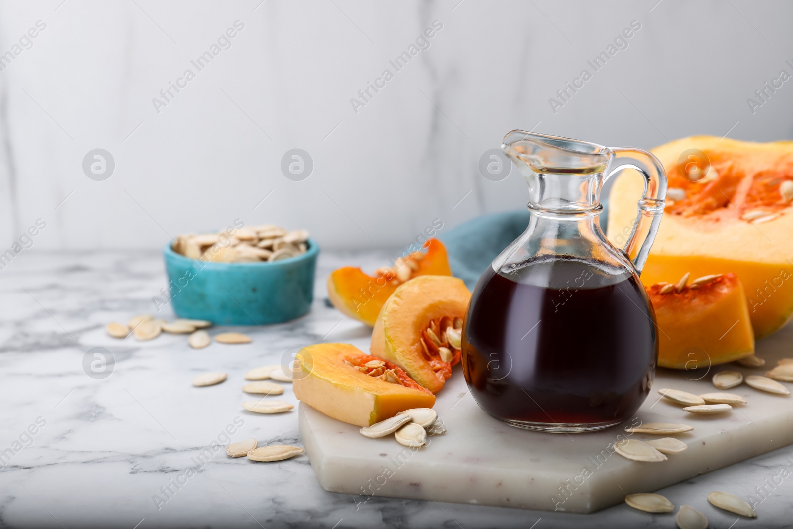 Photo of Fresh pumpkin seed oil in glass jug on white marble table. Space for text