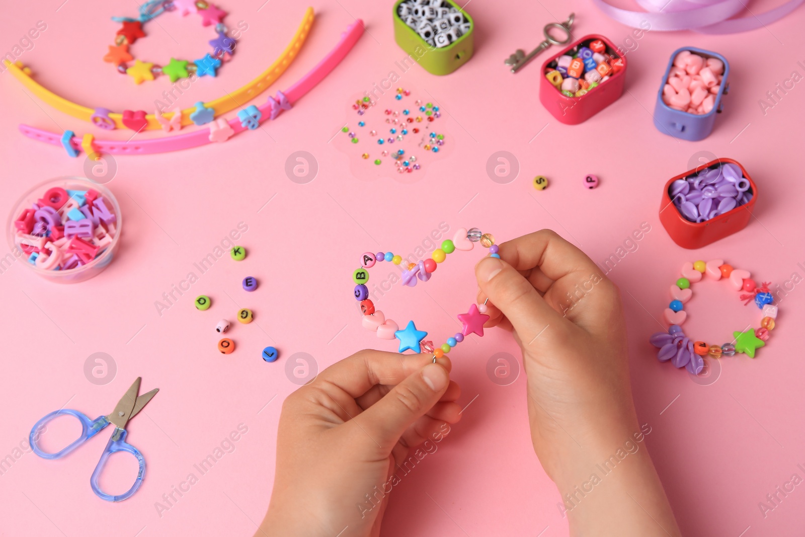 Photo of Child making beaded jewelry and different supplies on pink background, above view. Handmade accessories