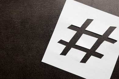 Photo of White paper stencil with symbol of hashtag on dark background, top view. Space for text