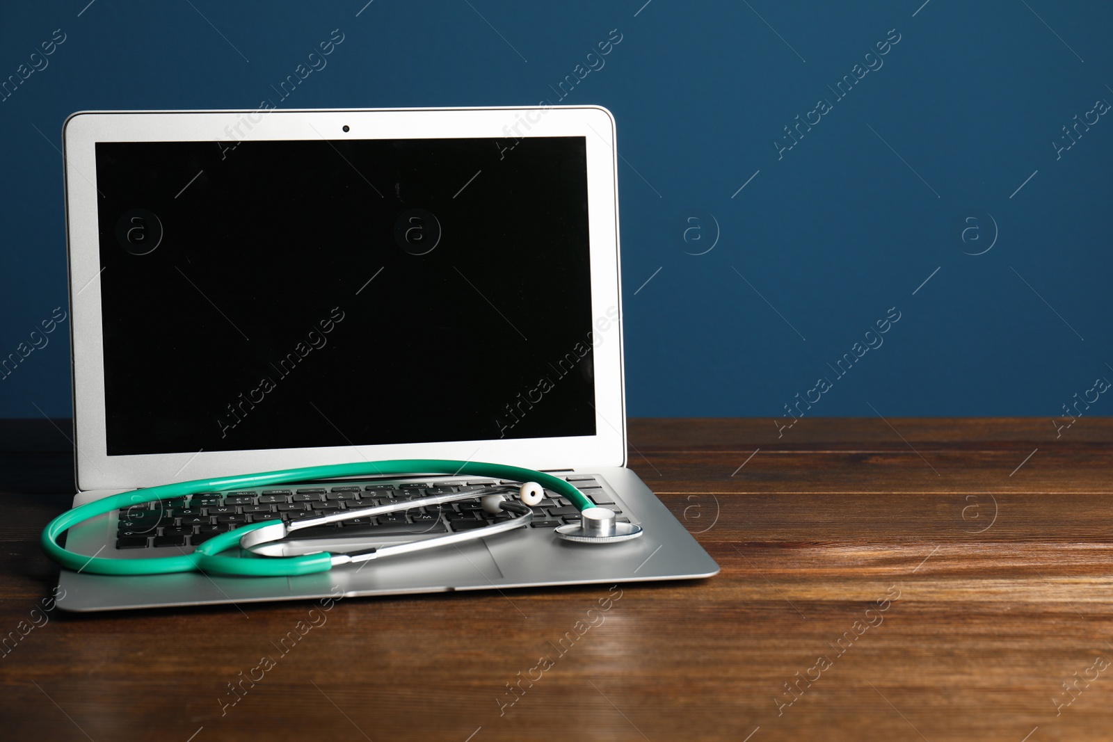 Photo of Modern laptop with stethoscope on table against color wall. Mockup for design