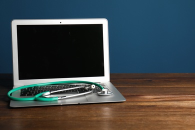 Modern laptop with stethoscope on table against color wall. Mockup for design