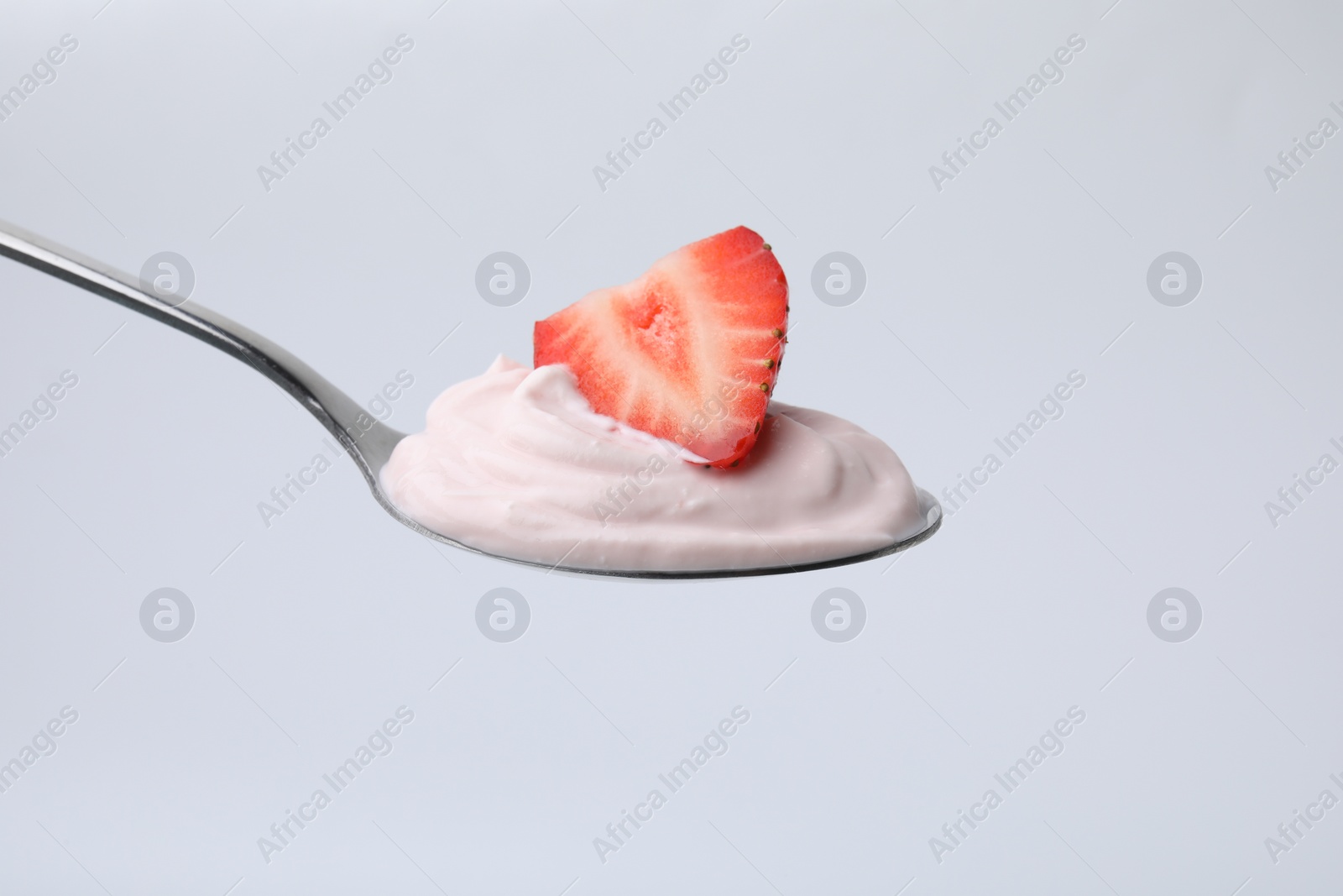 Photo of Delicious natural yogurt with fresh strawberry in spoon on light background