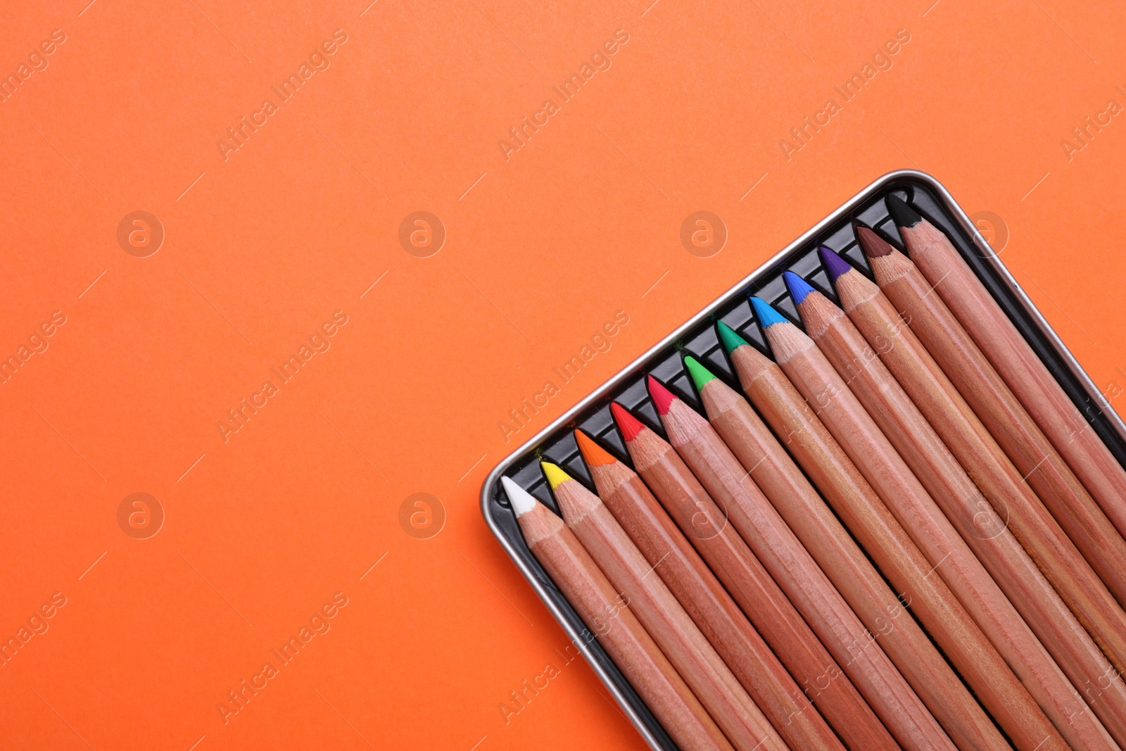 Photo of Box with many colorful pastel pencils on orange background, top view and space for text. Drawing supplies