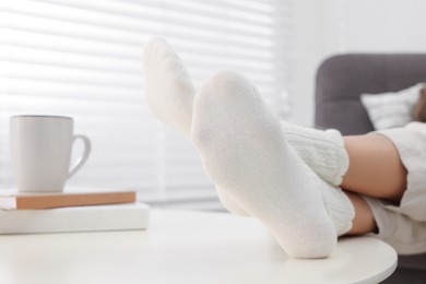 Woman in warm socks relaxing near table at home, closeup. Space for text