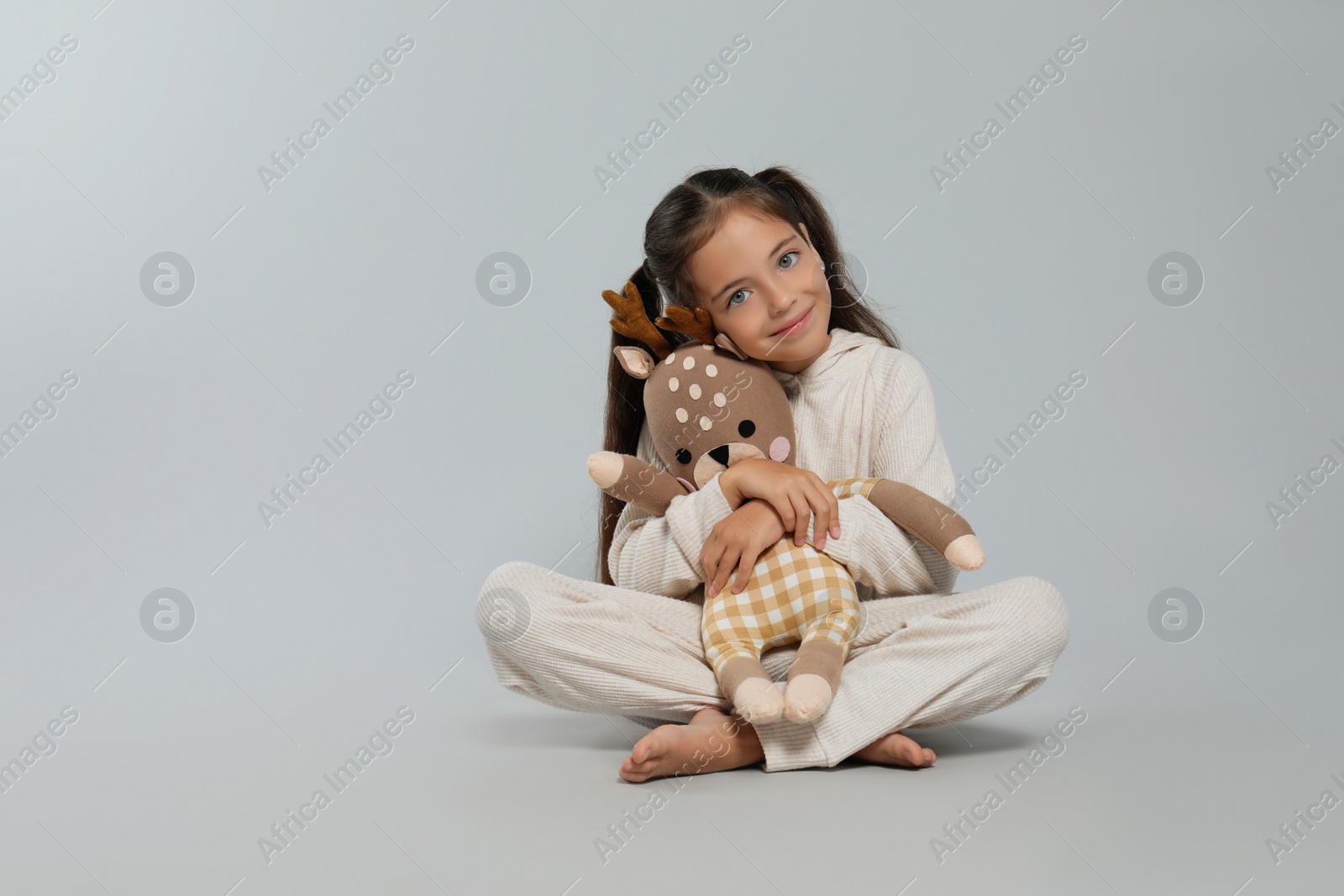 Photo of Cute girl in white pajamas with toy deer on light grey background. Space for text