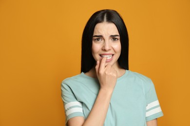 Photo of Young woman biting her nails on yellow background