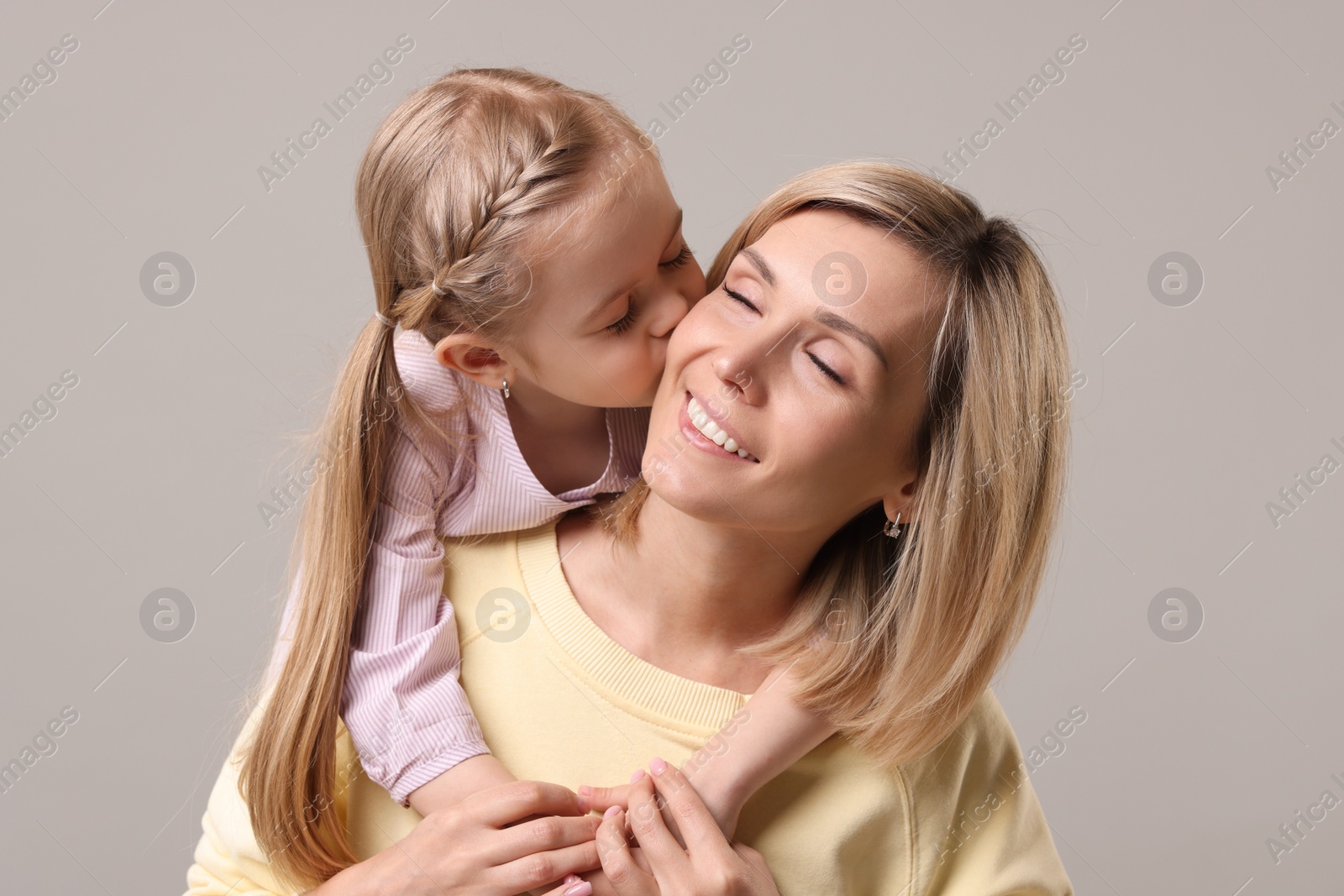 Photo of Daughter kissing her happy mother on grey background