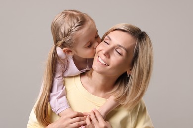 Daughter kissing her happy mother on grey background