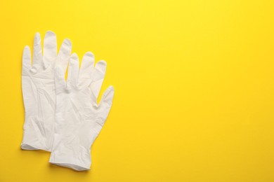 Photo of Pair of medical gloves on yellow background, flat lay. Space for text