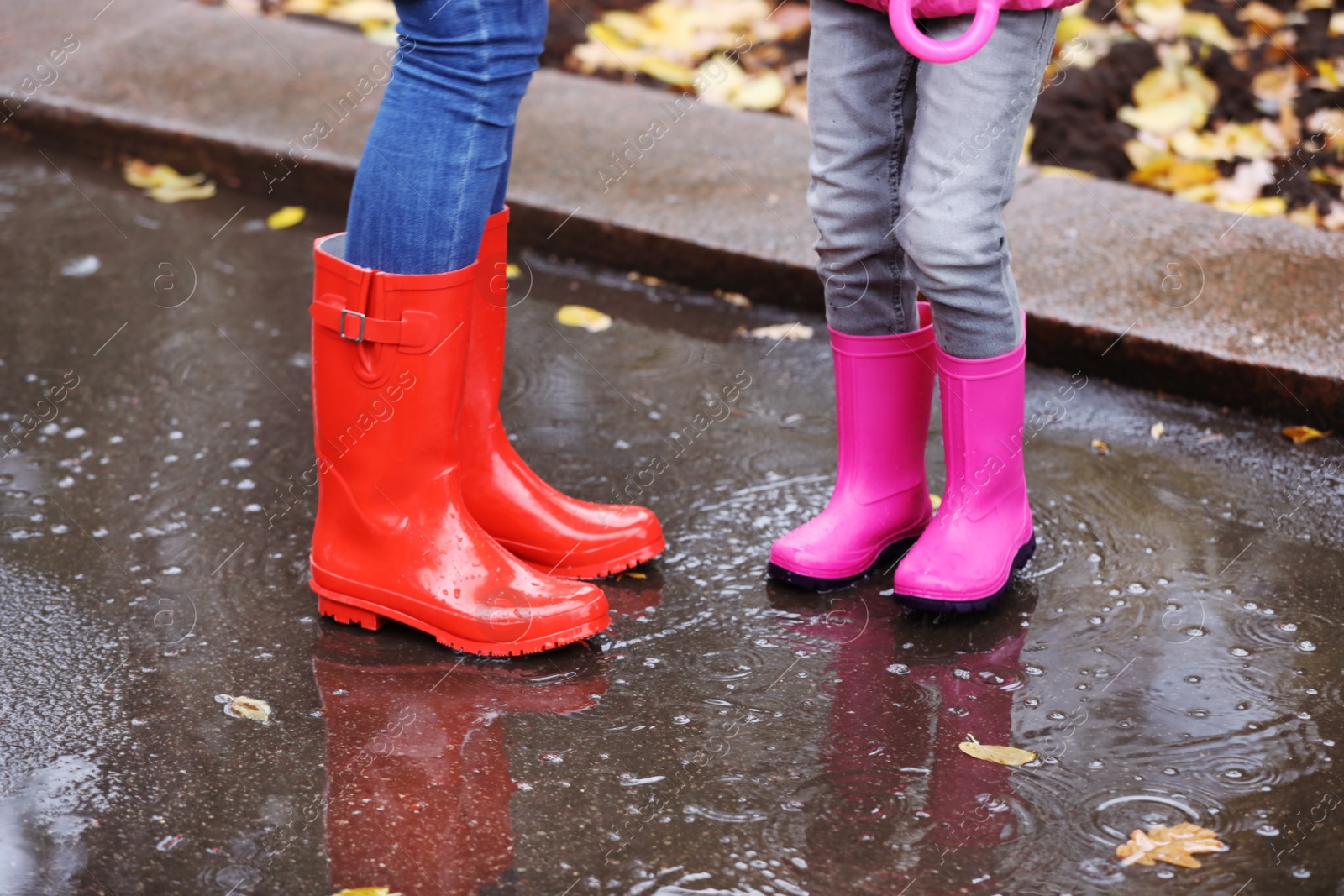 Photo of Mother and daughter wearing rubber boots standing in puddle on rainy day, focus of legs. Autumn walk