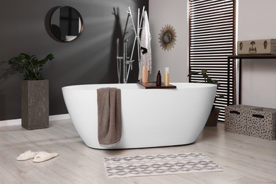 Photo of Stylish bathroom interior with ceramic tub, cosmetic products and houseplants