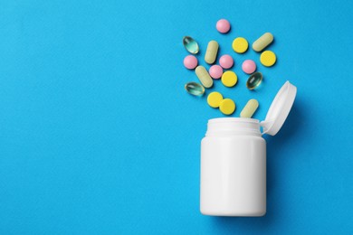 Photo of Different vitamin pills and bottle on light blue background, top view. Space for text