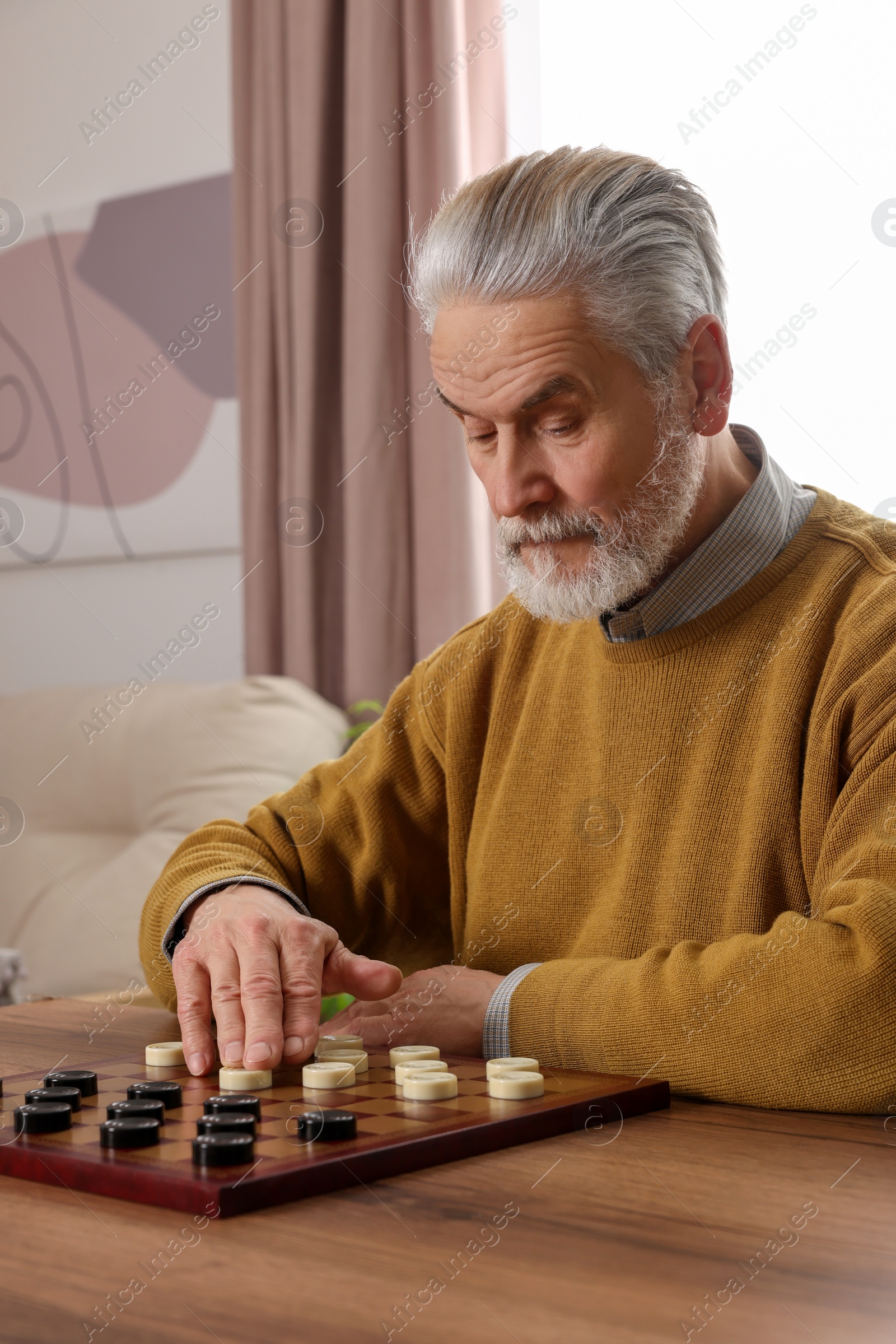 Photo of Playing checkers. Concentrated senior man thinking about next move at table in room