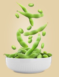 Fresh edamame soybeans and pods falling into bowl on beige background