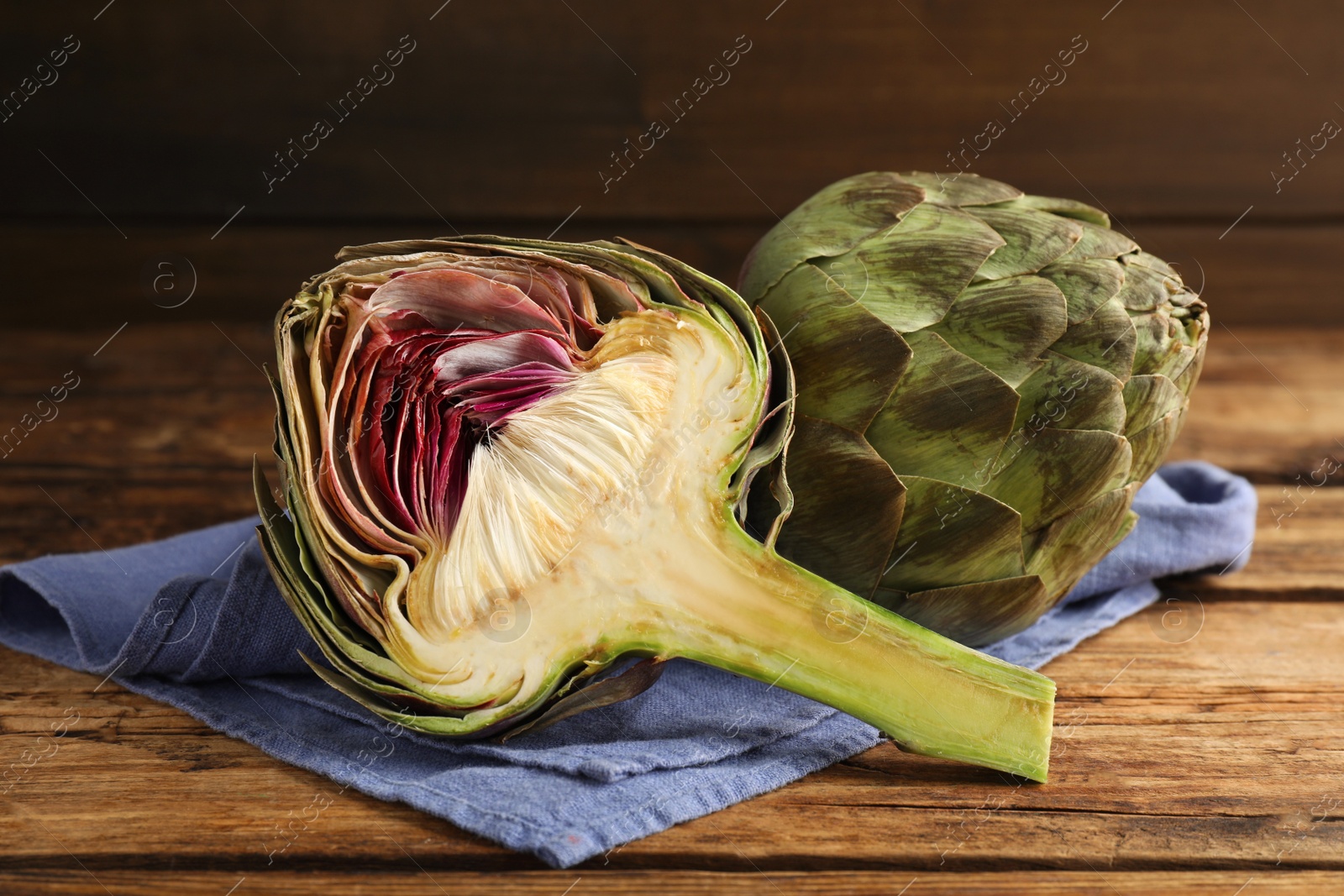 Photo of Cut and whole fresh raw artichokes on wooden table