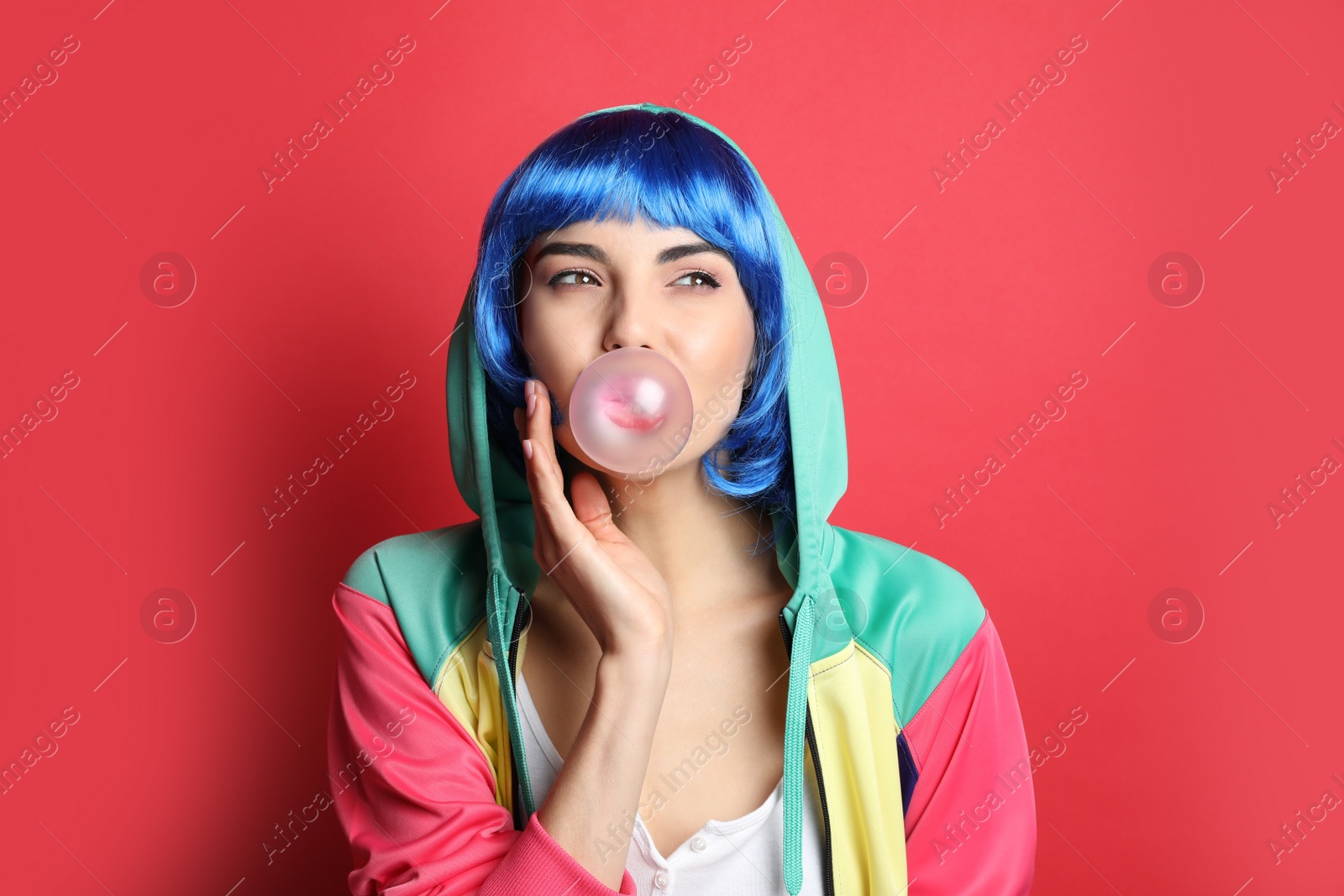 Photo of Fashionable young woman in colorful wig blowing bubblegum on red background