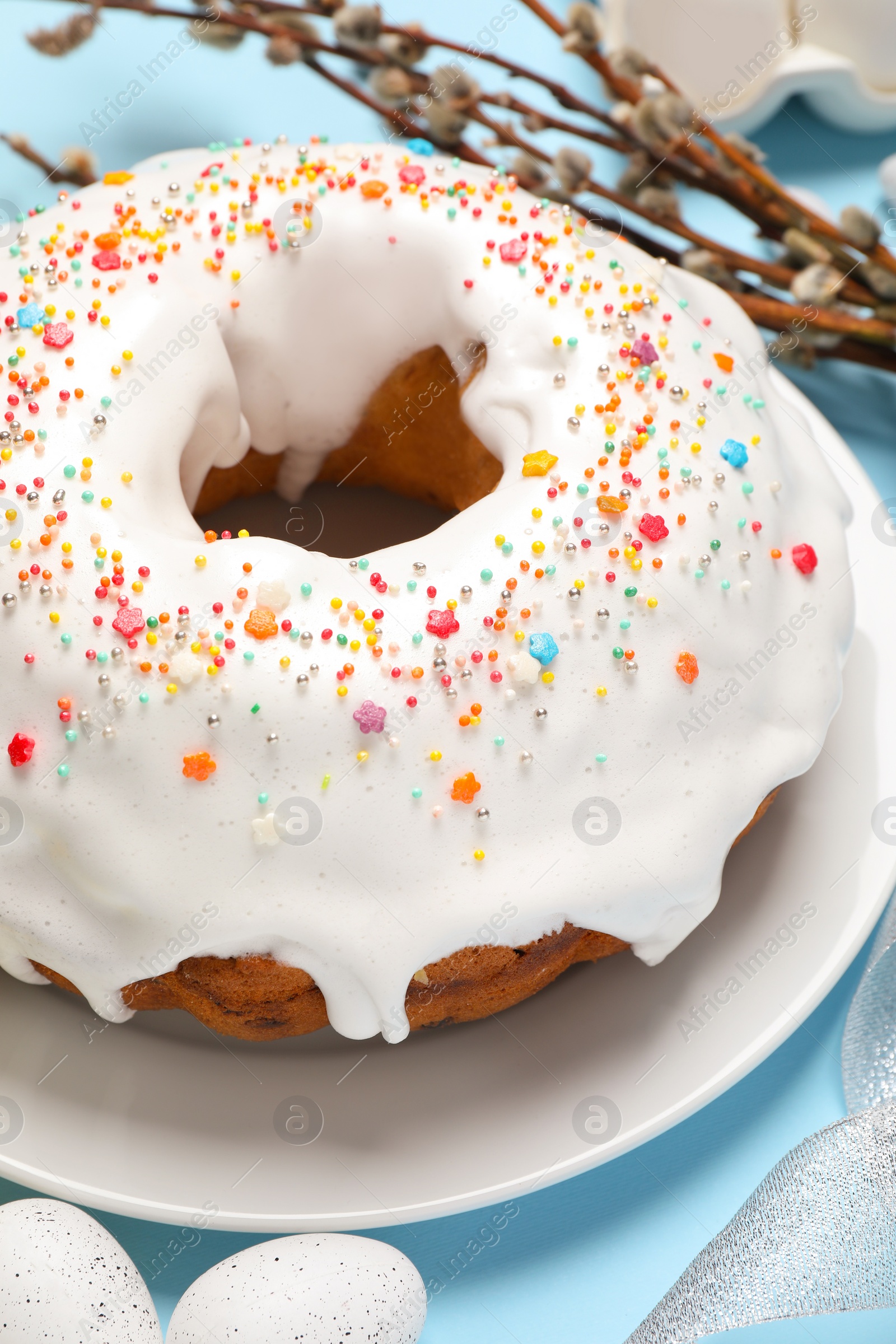 Photo of Delicious Easter cake decorated with sprinkles near painted eggs and willow branches on light blue background