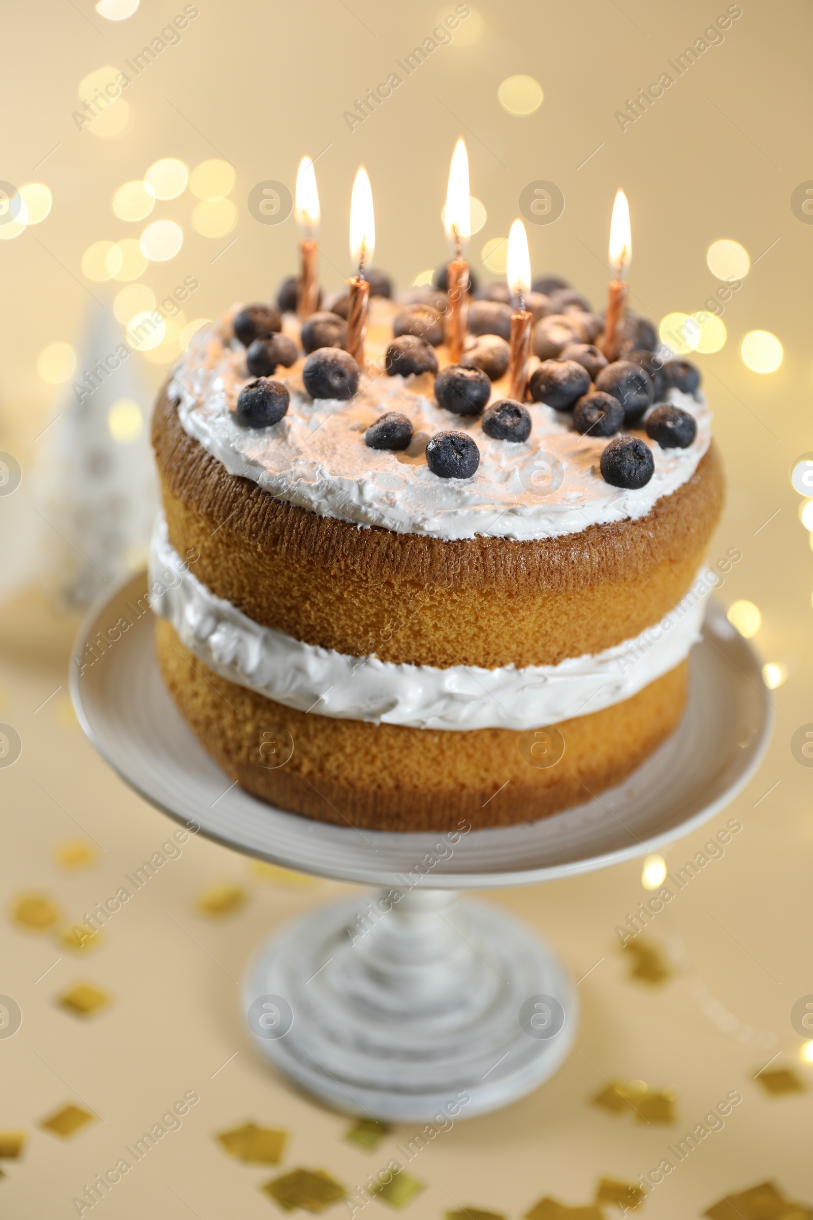 Photo of Tasty cake with burning candles on beige background against blurred lights