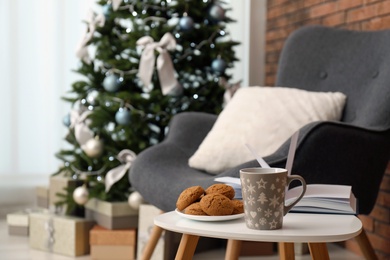 Photo of Book with treat on table and Christmas tree in stylish living room interior