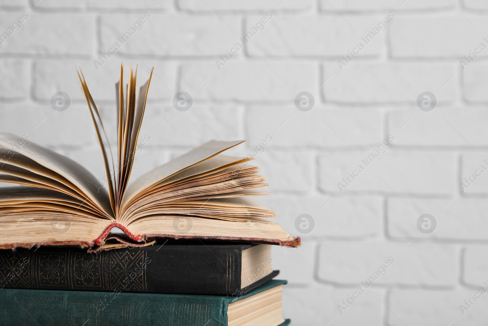 Photo of Many old hardcover books near white brick wall, closeup. Space for text