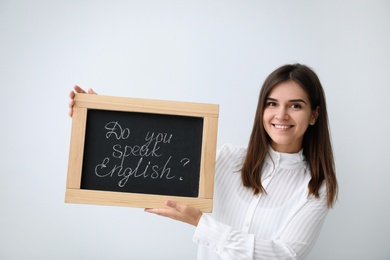 Photo of Young female teacher holding chalkboard with words DO YOU SPEAK ENGLISH? on light background
