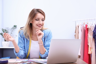 Beautiful young stylist at workplace near rack with clothes