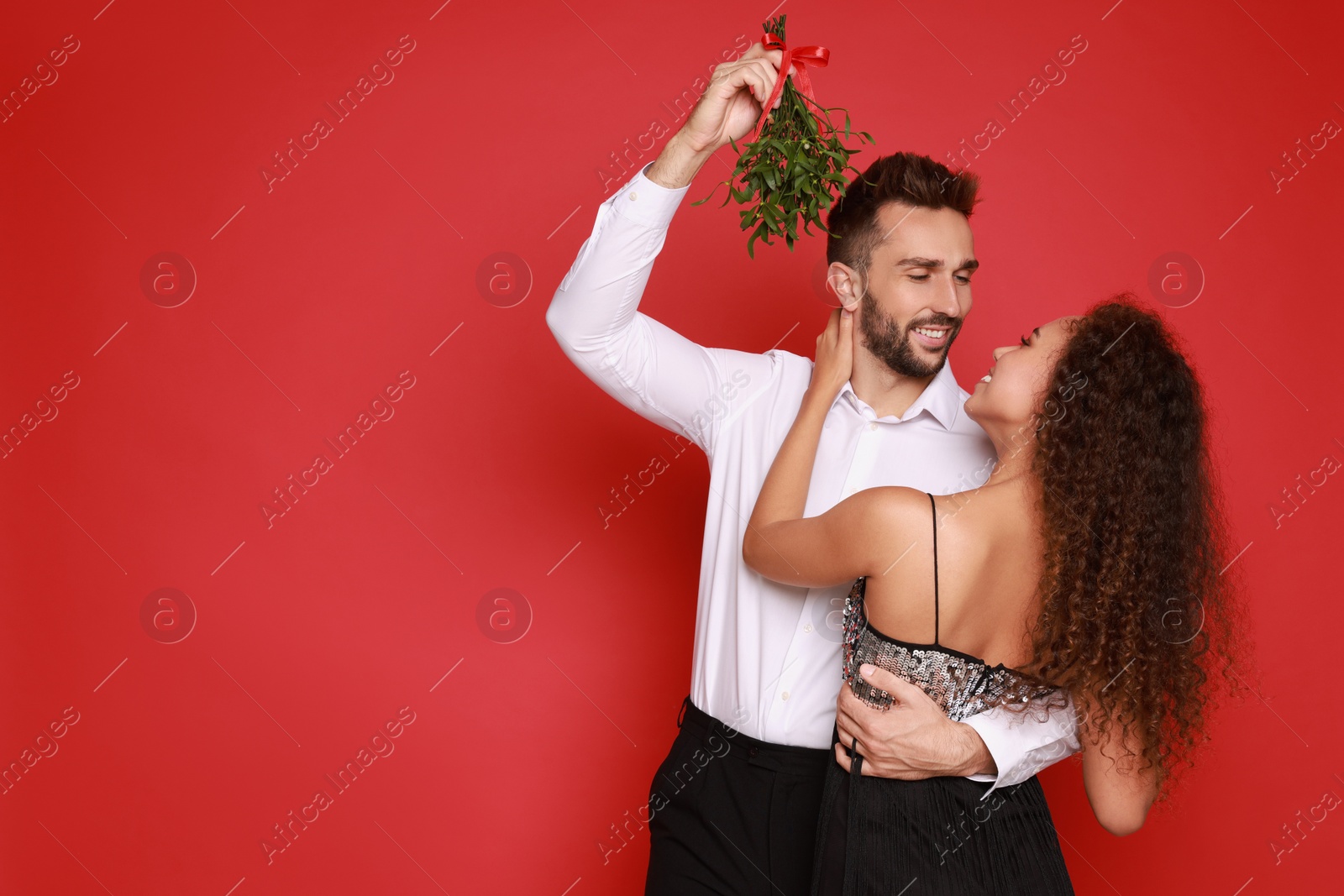 Photo of Lovely couple under mistletoe bunch on red background. Space for text