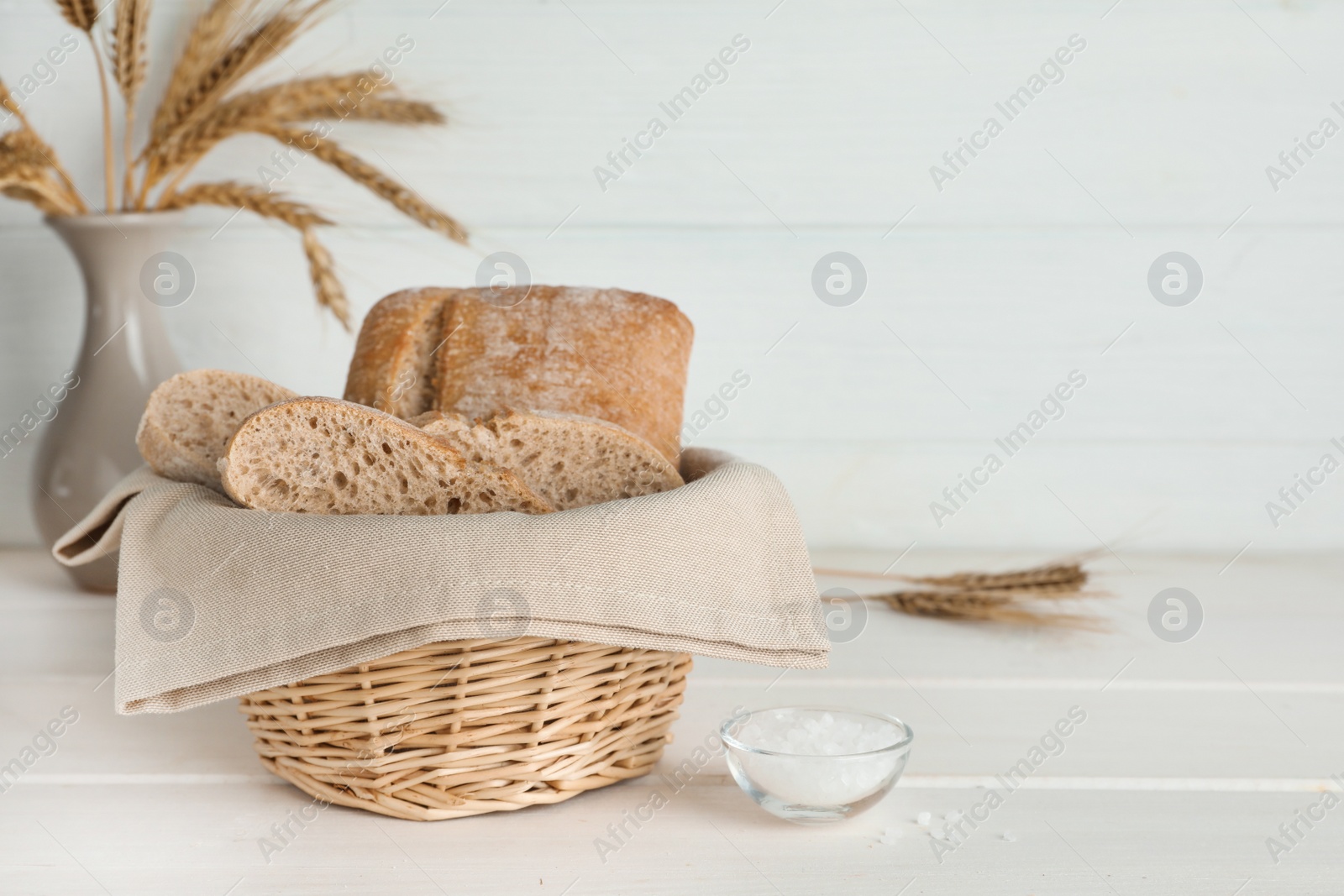 Photo of Cut delicious ciabatta in wicker basket and on beige wooden table, space for text