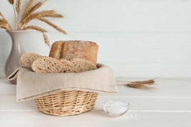 Cut delicious ciabatta in wicker basket and on beige wooden table, space for text