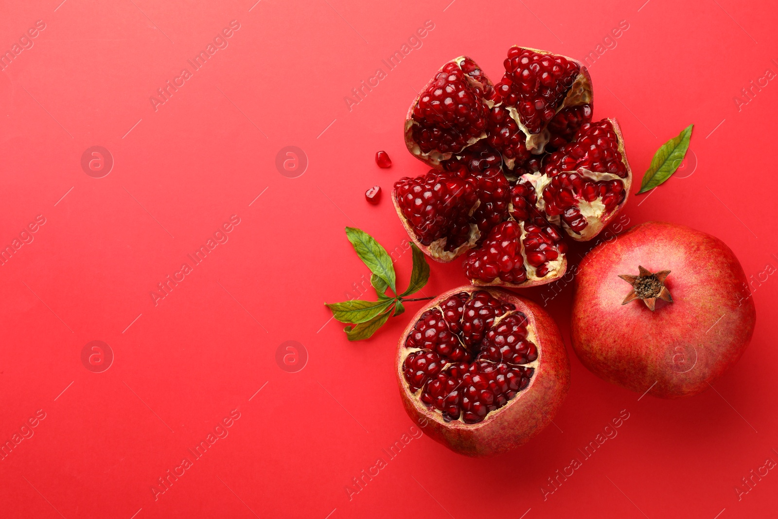 Photo of Fresh pomegranates and green leaves on red background, flat lay. Space for text