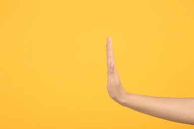 Photo of Woman showing stop gesture on orange background, closeup. Space for text