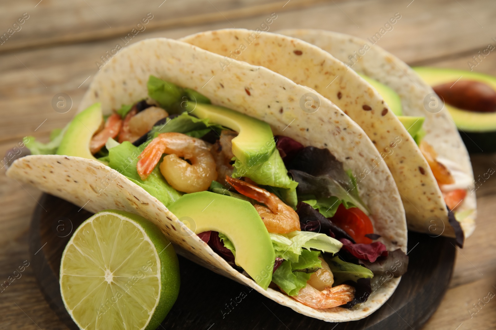 Photo of Delicious tacos with shrimps, avocado and lime on wooden table, closeup