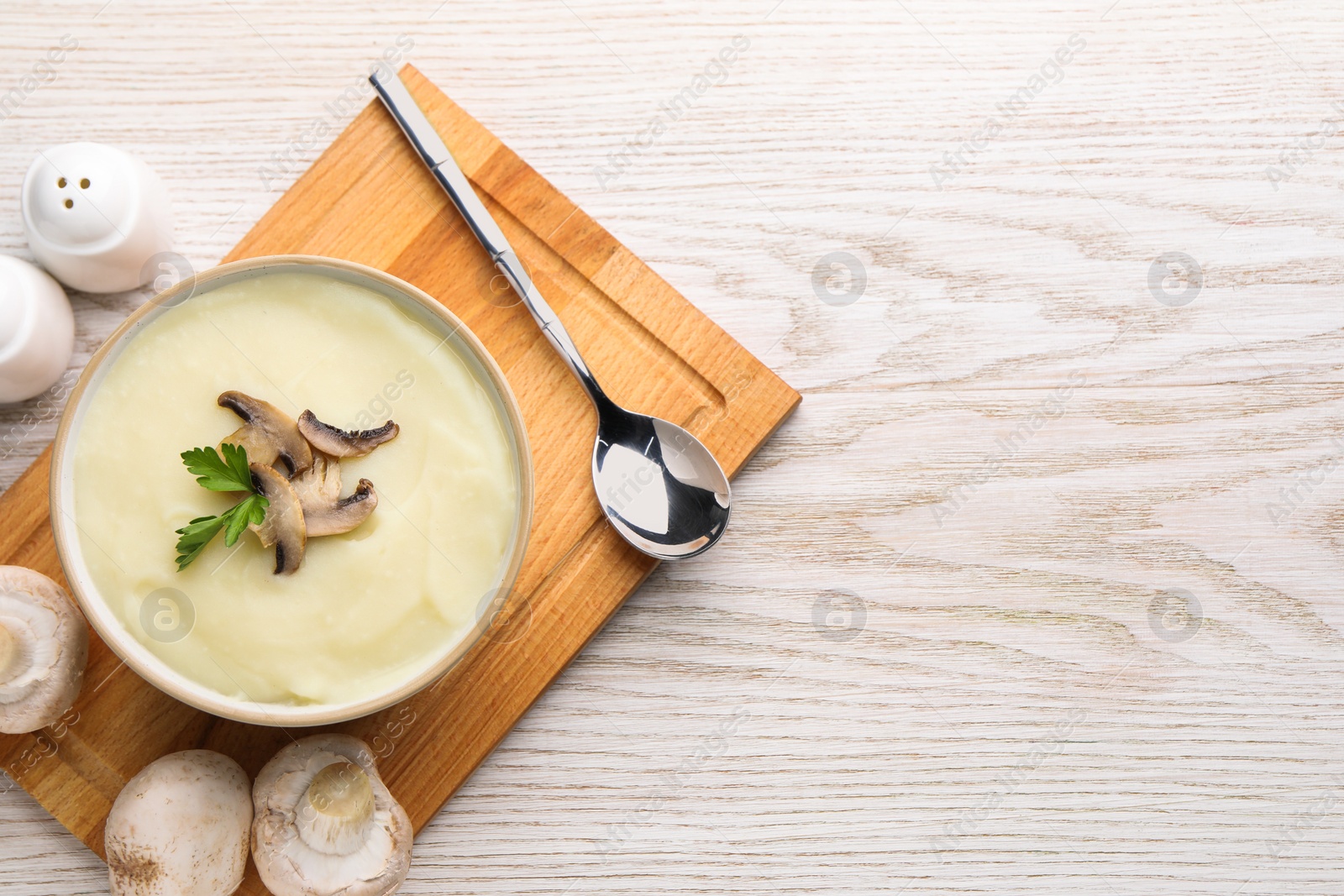 Photo of Bowl of tasty cream soup with mushrooms, parsley and spoon on light wooden table, flat lay. Space for text