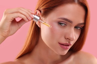 Photo of Beautiful young woman applying cosmetic serum onto her face on pink background, closeup
