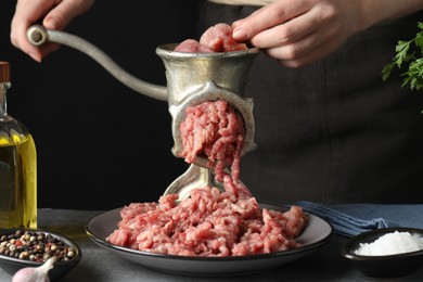 Photo of Woman making beef mince with manual meat grinder at grey table, closeup