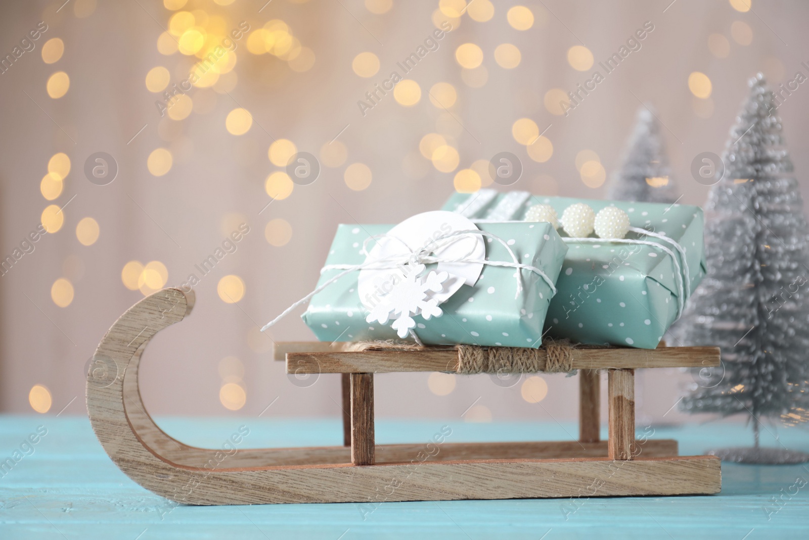 Photo of Sleigh with gift boxes on turquoise wooden table against blurred lights