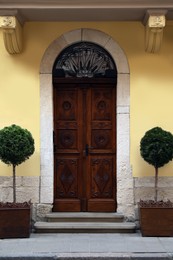 View of house with beautiful arched wooden door and potted trees. Exterior design