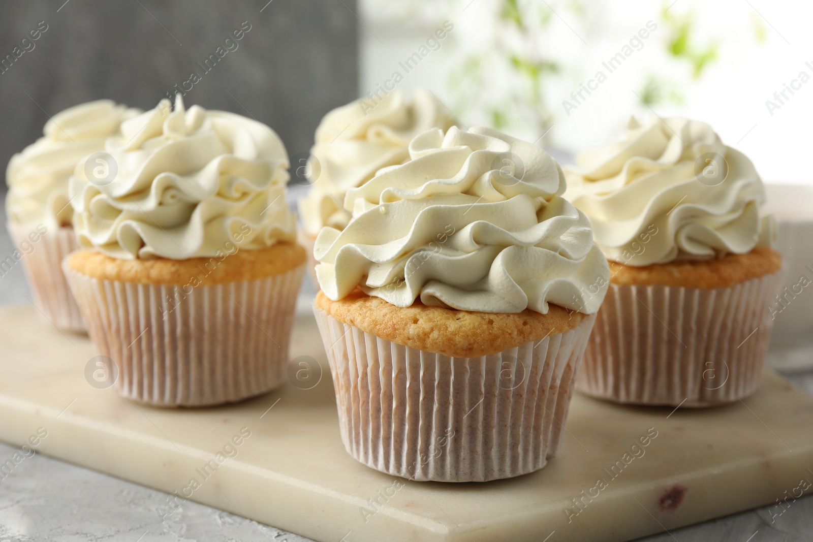 Photo of Tasty cupcakes with vanilla cream on grey table, closeup