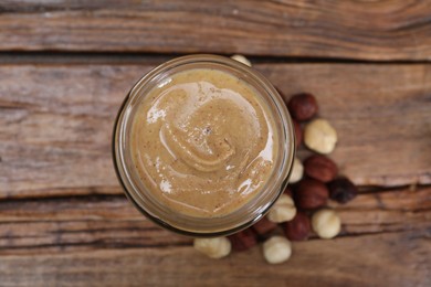 Photo of Tasty hazelnut nut paste in jar on wooden table, top view