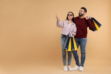 Happy couple with shopping bags looking at something on beige background. Space for text