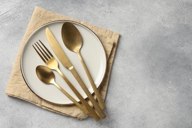 Stylish cutlery, plate and napkin on light grey table, top view. Space for text