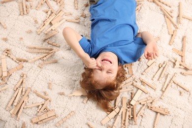 Photo of Cute little boy surrounded by wooden construction set on carpet at home, top view. Child`s toy
