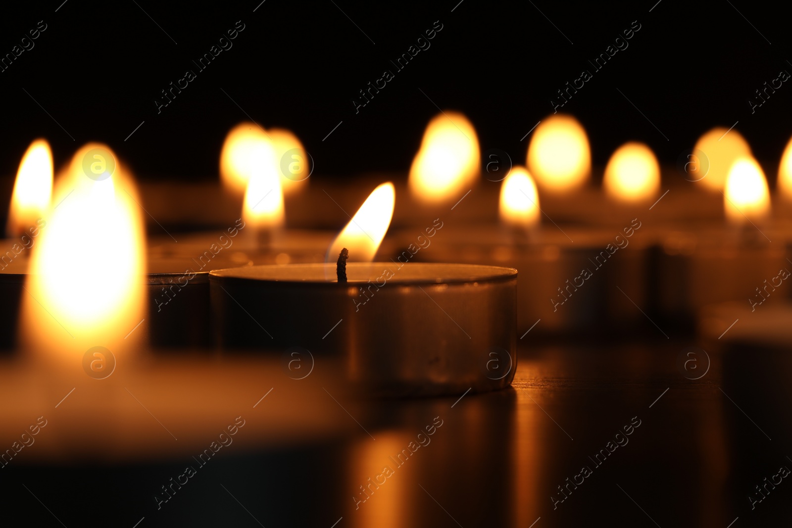 Photo of Burning tealight candles on dark surface, closeup