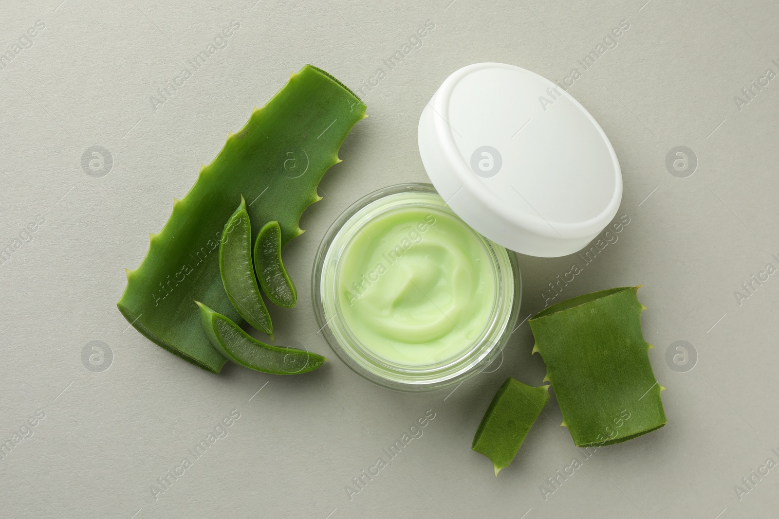 Photo of Jar with cream and cut aloe leaves on light grey background, flat lay