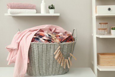 Photo of Wicker basket with dirty laundry and clothespins on table indoors