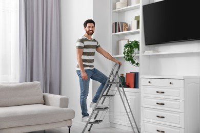 Happy man on metal folding ladder at home