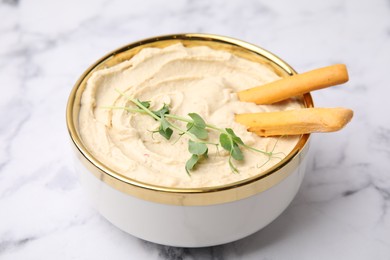 Delicious hummus with grissini sticks on white marble table, closeup