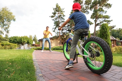 Photo of Dad teaching son to ride bicycle outdoors