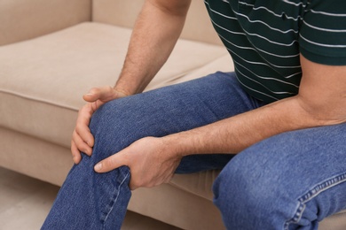 Photo of Senior man suffering from knee pain at home, closeup