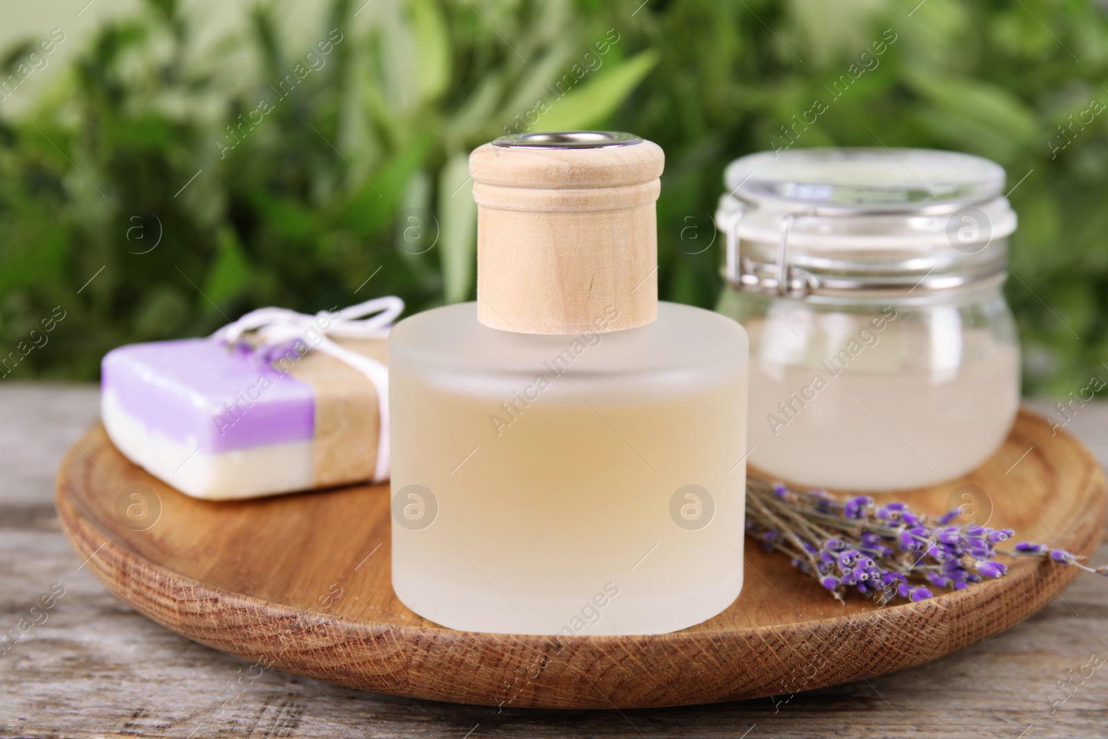 Photo of Natural herbal oil and lavender flowers on table against blurred background